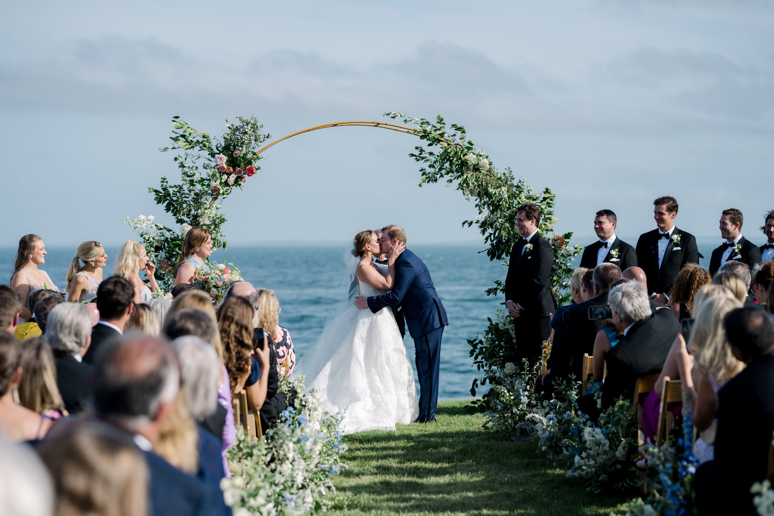bride-and-groom-kiss-under-arch-along-the-ocean