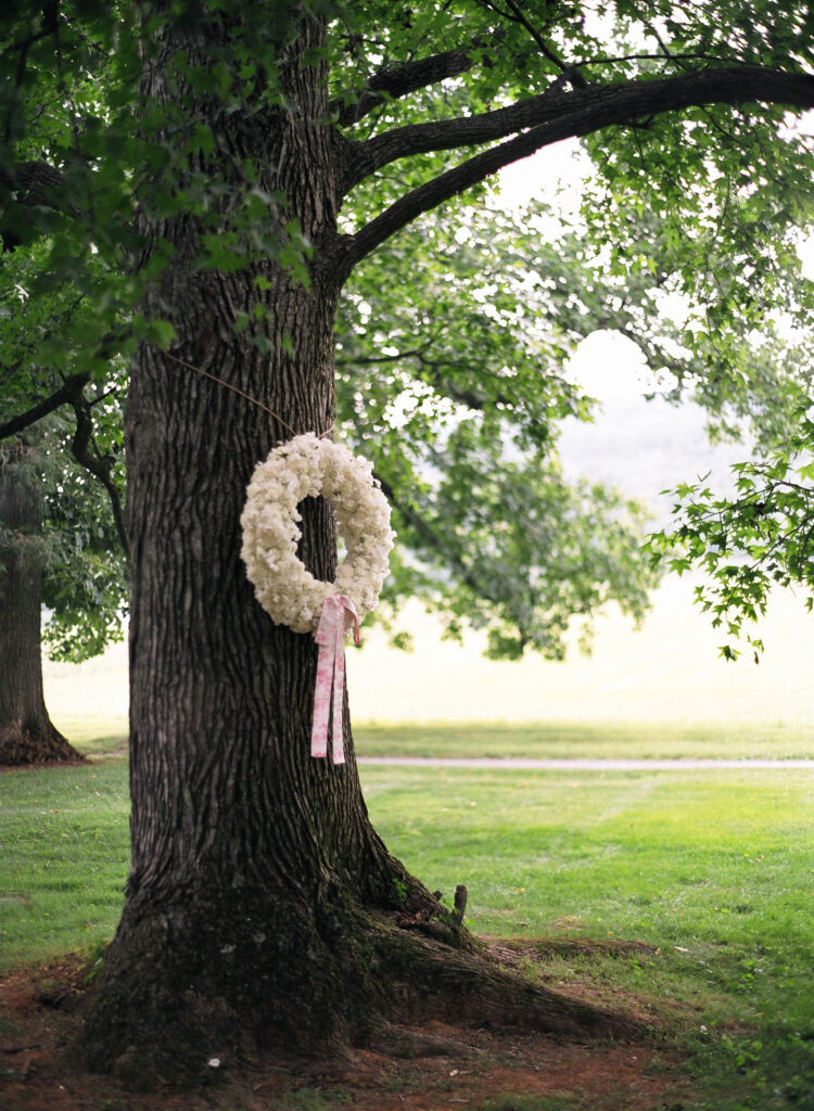 white-floral-wreath-hanging-on-tree-at-outdoor-wedding